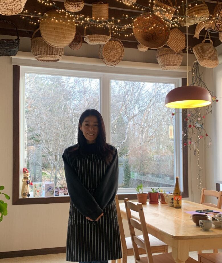 A woman stands next to a dining table with tiny lights and baskets hanging from the ceiling.