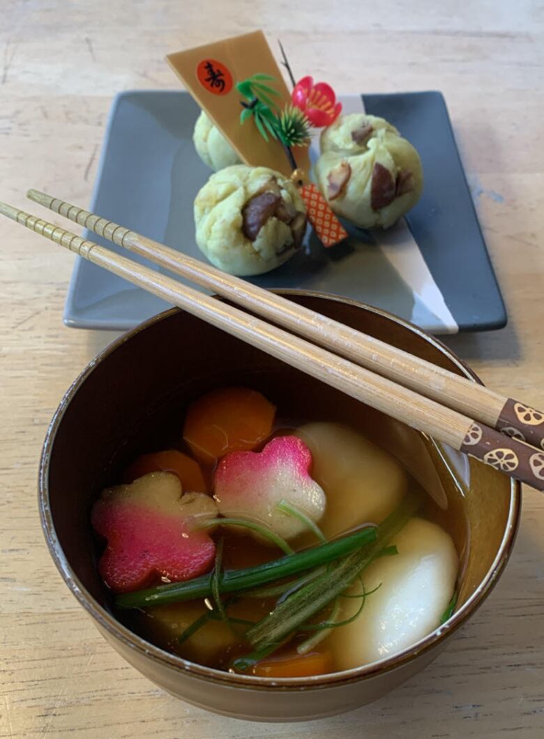 A small bowl of soup with chopsticks and small items on a plate.