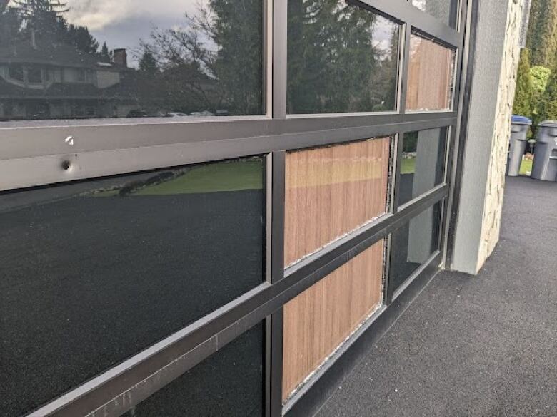 A garage door with at least one bullet hole and four shattered glass panels.