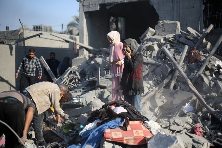 A child covers their face while standing amid rubble as other search through the debris.