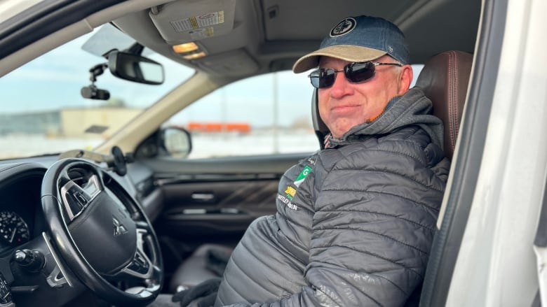 A man is sitting in the driver seat of a vehicle and looking at the camera.