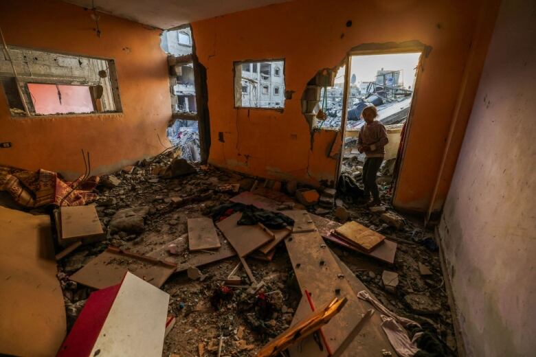 A girl stands at the door of a house destroyed in Israeli bombardment.