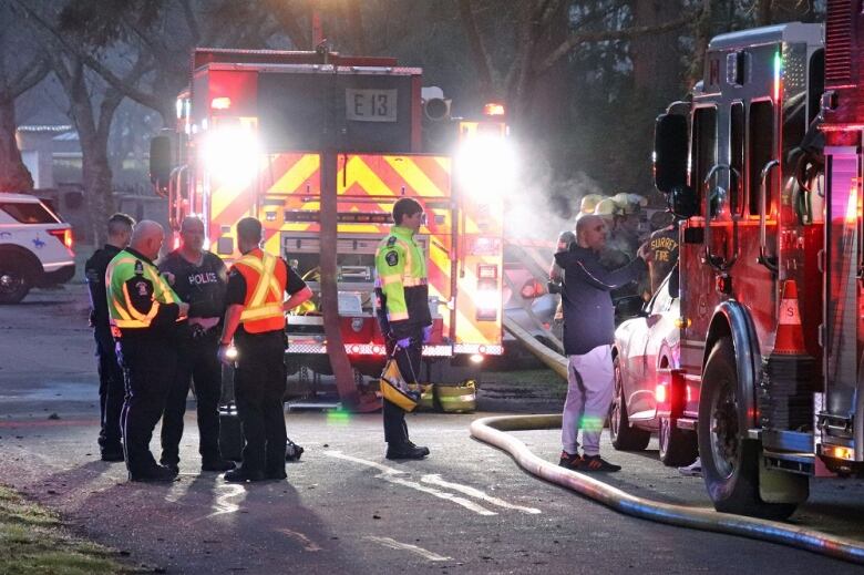 Emergency responders and some civilians stand around multiple fire trucks in early morning darkness.