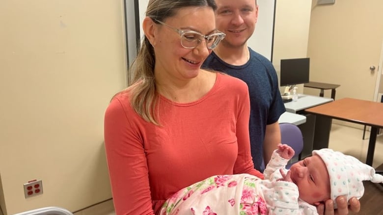 A woman holding a baby and a man standing behind her