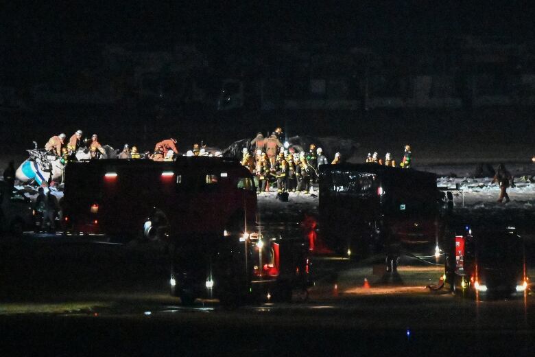 Firefighters and rescue crew work at the site where two aircraft collided on the tarmac, at night, with vehicles in the foreground.