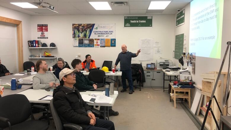 A group of about 10 people looks at a presentation on a screen that the instructor is pointing at.