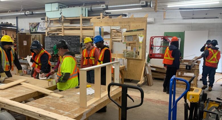 A group of people in reflective vests crowd around a table to cut a two-by-four with.