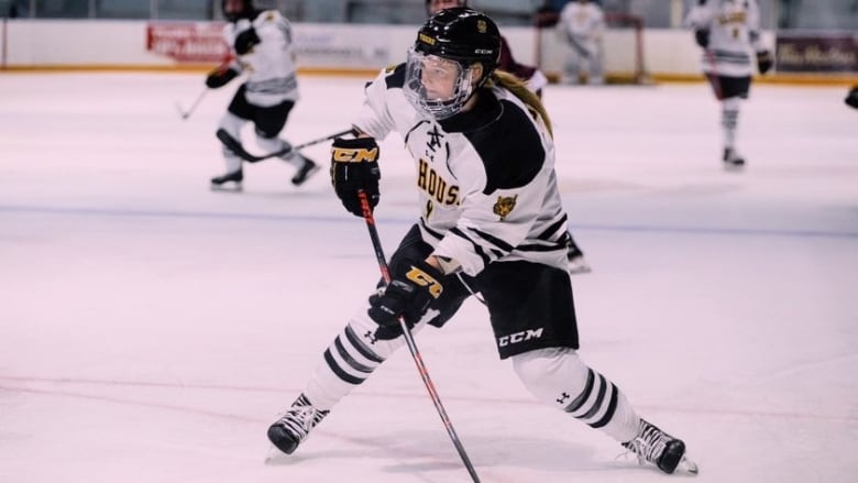 A hockey player is carrying the puck forward on the ice. She's wearing a Dalhousie jersey and a helmet.