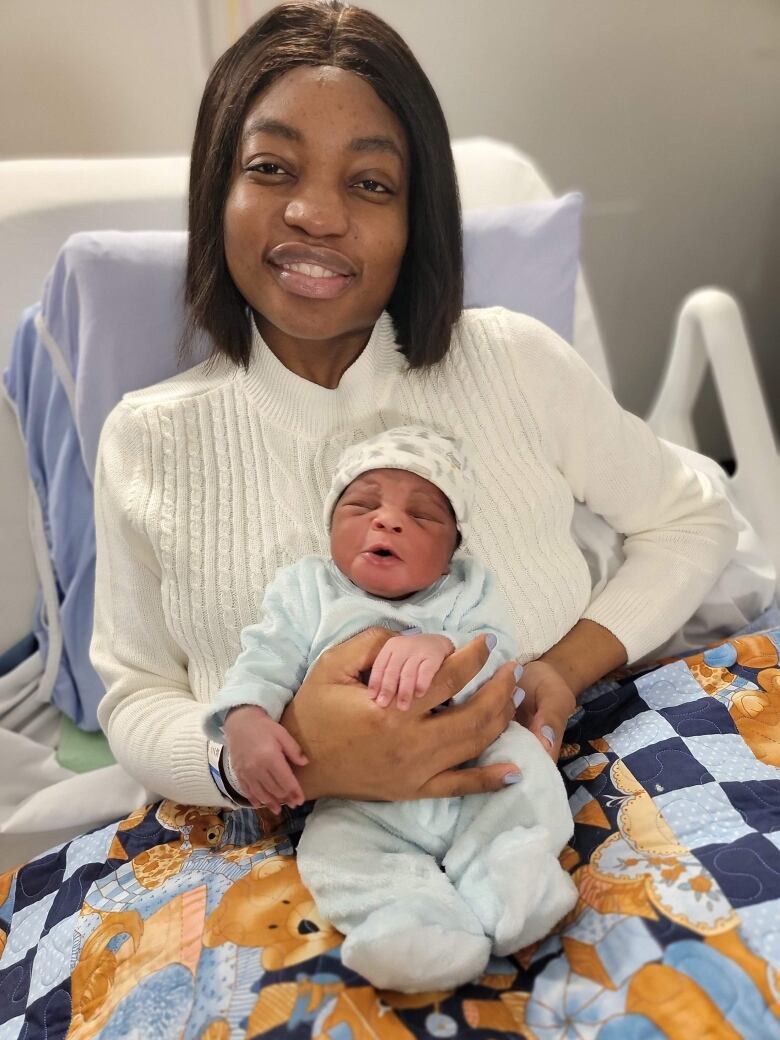 A Black woman holds up a newborn child who is crying in a hospital bed.