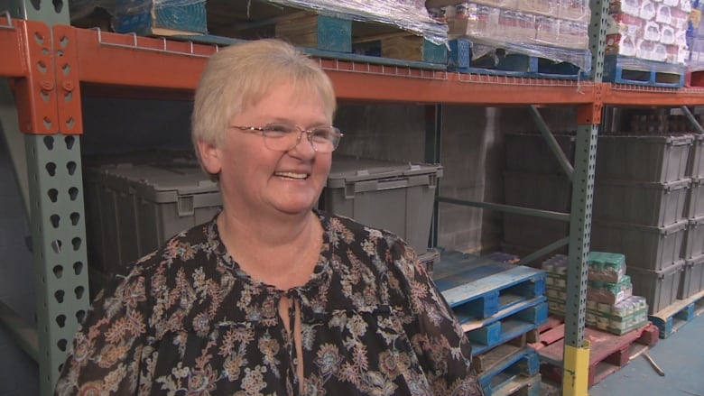 A smiling woman with short blonde hair and glasses stands in a warehouse.