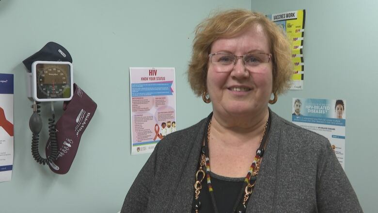 Marilyn Barrett smiles facing the camera in an examination room. Posters line the walls behind her.