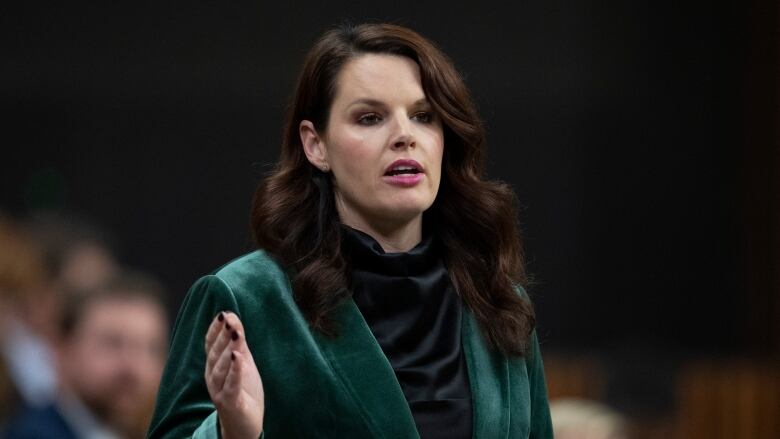 A woman wearing a green blazer speaks in the House of Commons.