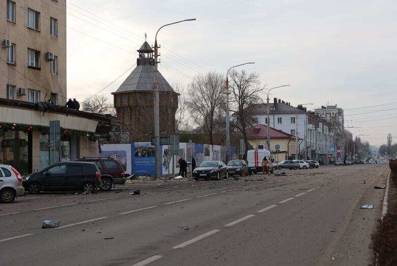 Debris is scattered on a street lined by cars with a wooden church steeple in the background