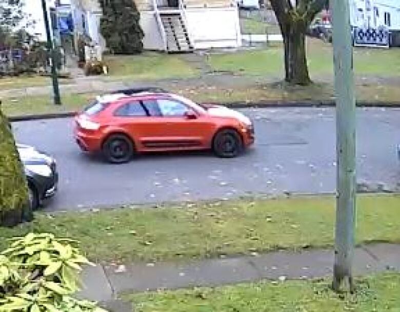 An orange car drives along a suburban street.