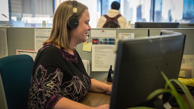 A woman wears a headset and looks at a computer monitor as she takes a call at Distress Centre Calgary