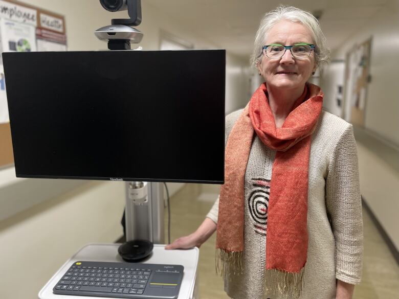 A woman stands next to a telemedicine cart. 