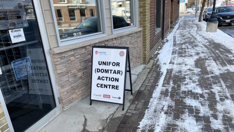 A sign that says Unifor Domtar Action Centre is set up outside a storefront on a sidewalk.