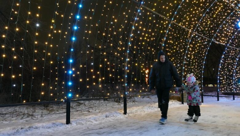 Two individuals walk and skate under a canopy of lights.