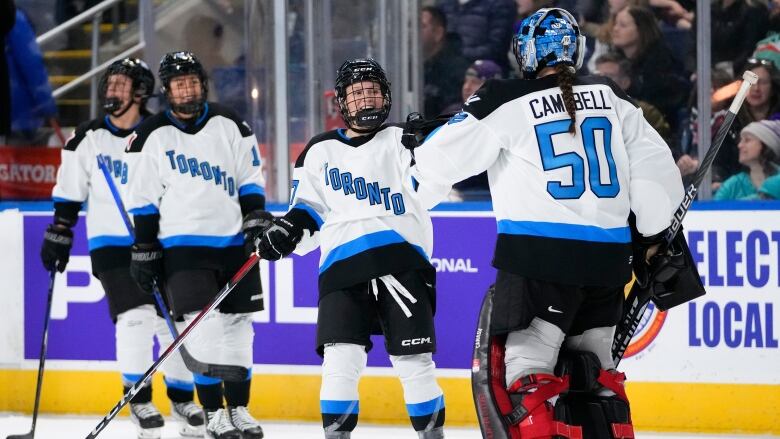 A female ice hockey player smiles while touching gloves with her team's goaltender in celebration during a game.