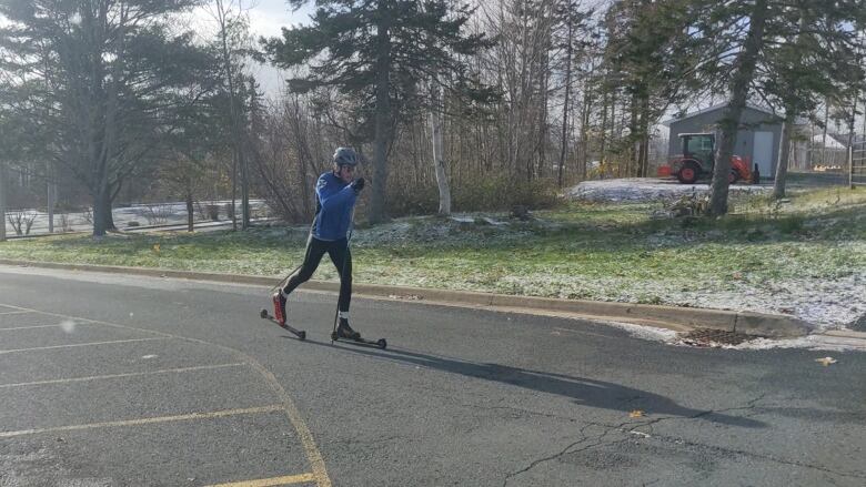 a man on two short roller skis on pavement. There is a skiff of snow on the ground, but you can still see grass. 