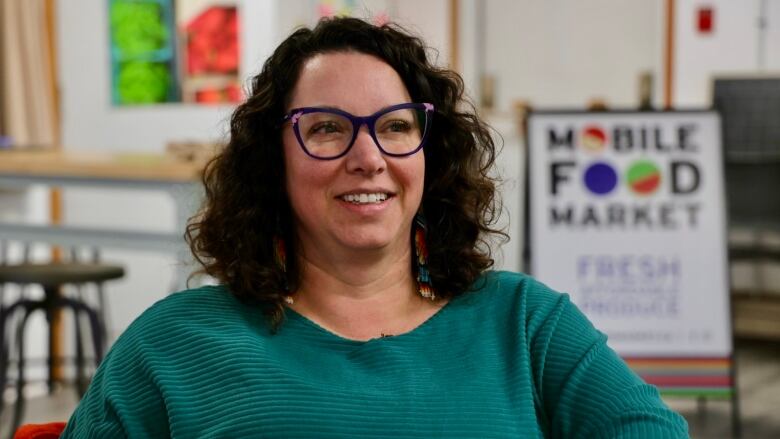 A woman with brown curly hair and glasses smiles and looks off to the side. 