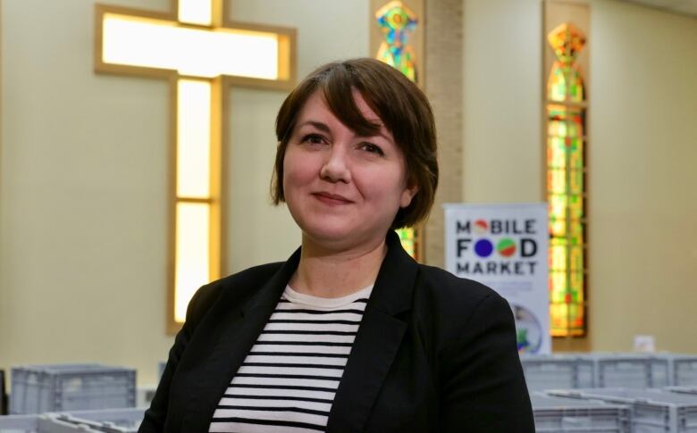 A woman with short brown hair smiles for the camera in a church. Behind her is a cross and a sign that reads, 'Mobile Food Market,' 