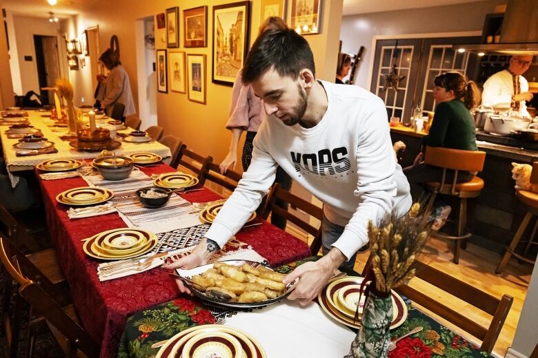 A man places a plate of cabbage rolls onto a dining room table.