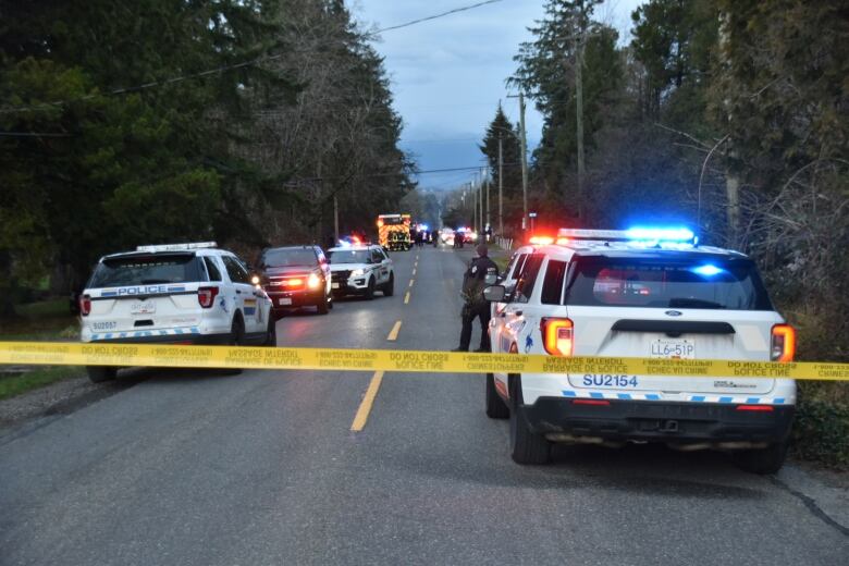 A long line of police vehicles on a road behind yellow police tape.