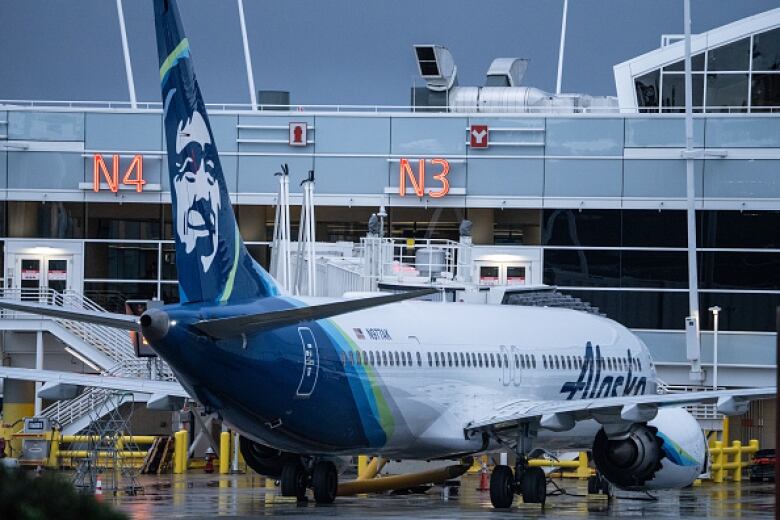 A large passenger airliner bearing the logo Alaska sits at at gate at an airport terminal.