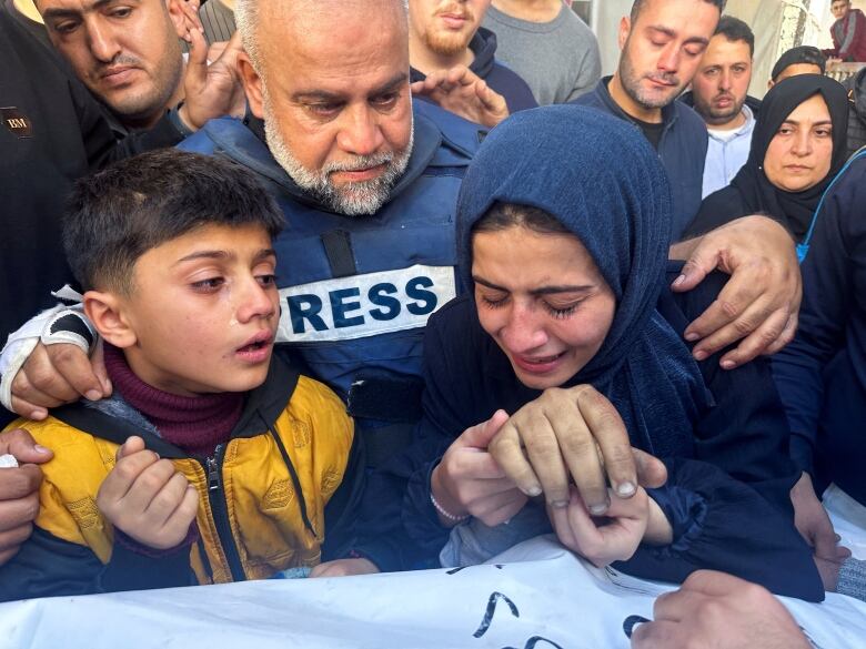 A bearded, grey-haired man with a blue vest that says 