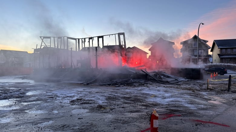 The framing of a house exposed by fire. The sun rises from the structure. Smoke rises from the exposed framing. 