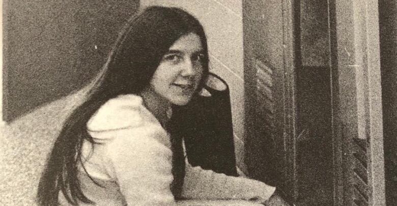 A person with long hair sits in a hihh school hallway near a locker