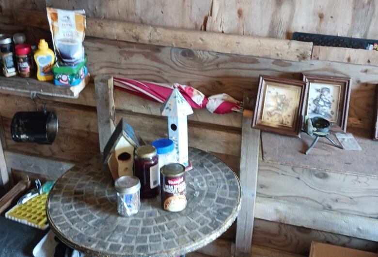 A small table with food and houseware items on it, with more kitchen and houseware items on a rough wood ledge behind it.