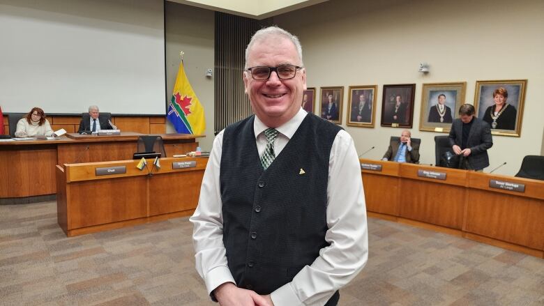 A man in dress clothes smiles as he poses for a photo.