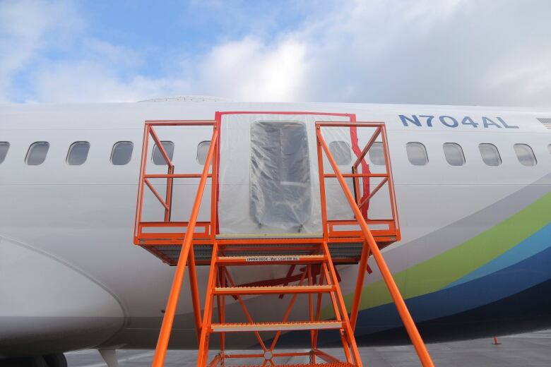 A portable staircase is shown up next against an airplane, which has tarp covering an open doorway.