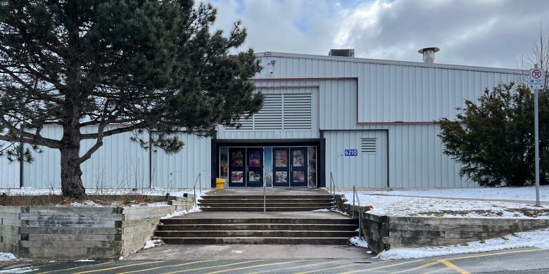 A set of wide stairs with a handrail leads from a parking lot to a building with grey siding. 