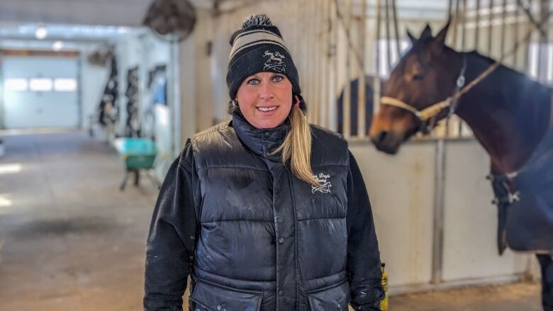 A woman in a toque and vest stands in a barn