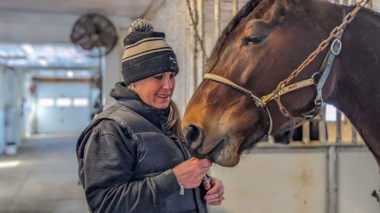 A woman gives a carrot to a horse as she smiles 