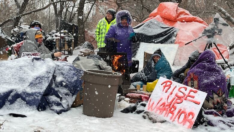 A group of people sit around a cluster of snowy tents and tarps. 