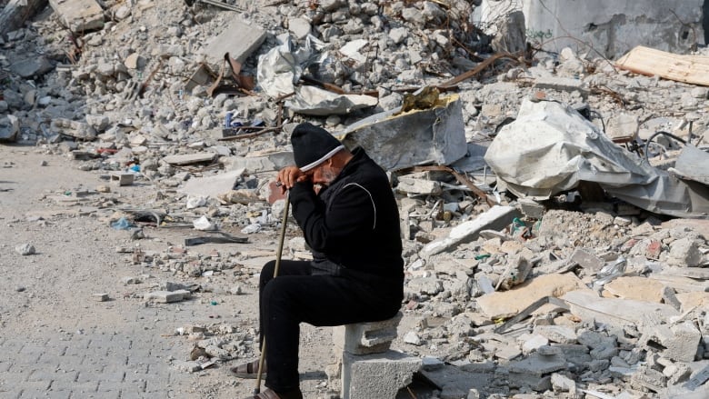 A man sits among rubble of a house destroyed by a missile.