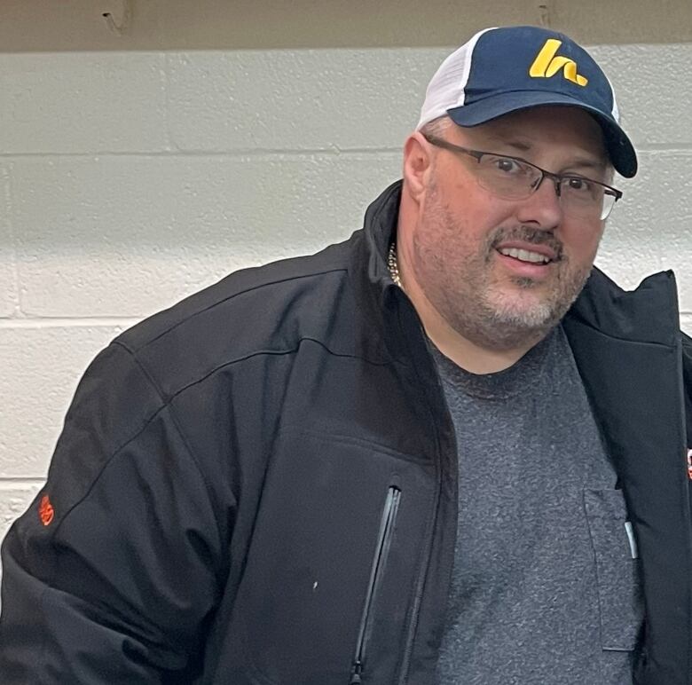 A smiling man wearing a baseball cap and a black windbreaker.