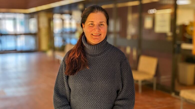 A woman in a grey sweater and ponytail stands in an open space at the farm centre. 