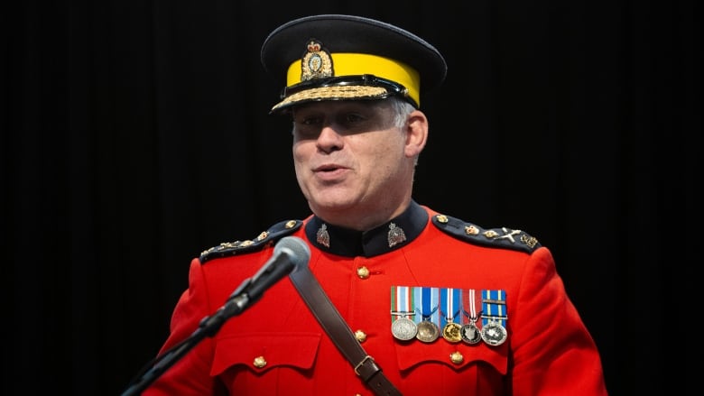 A man in a red police uniform stands behind a podium.