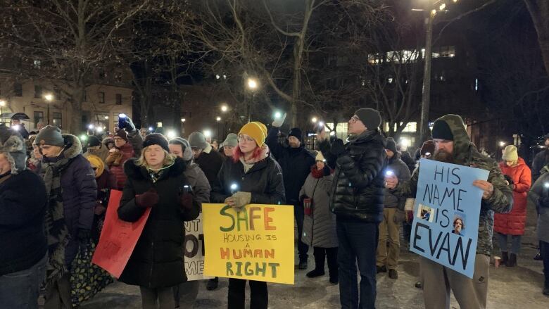 group of people with lit phones holding them up standing outside. Some holding signs.