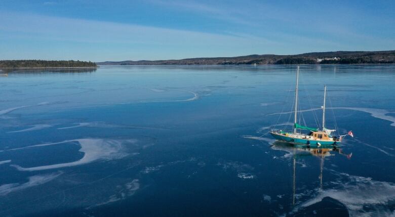 A double-masted sailboat is frozen into the ice on a body of water. 