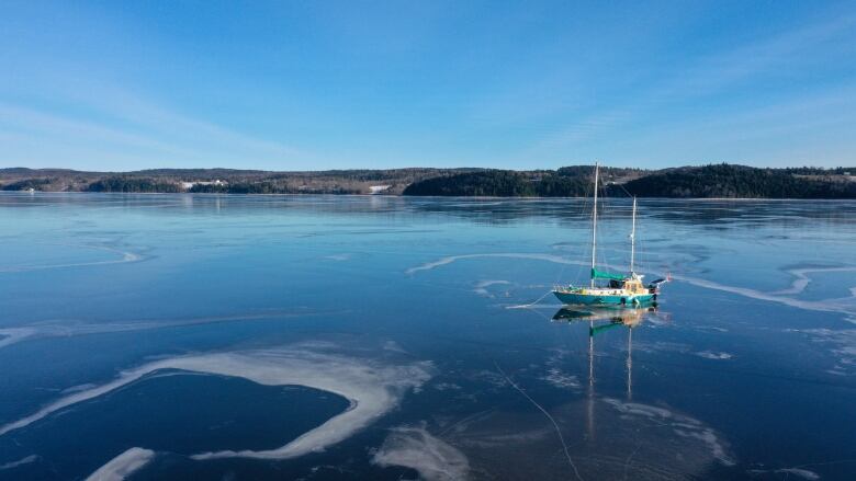 A double-masted sailboat is frozen into the ice on a body of water. 