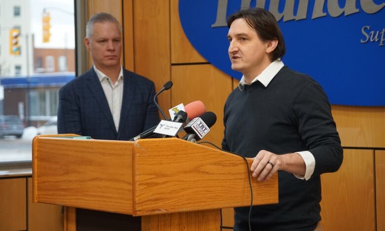 A person stands at a podium inside and speaks into a microphone.