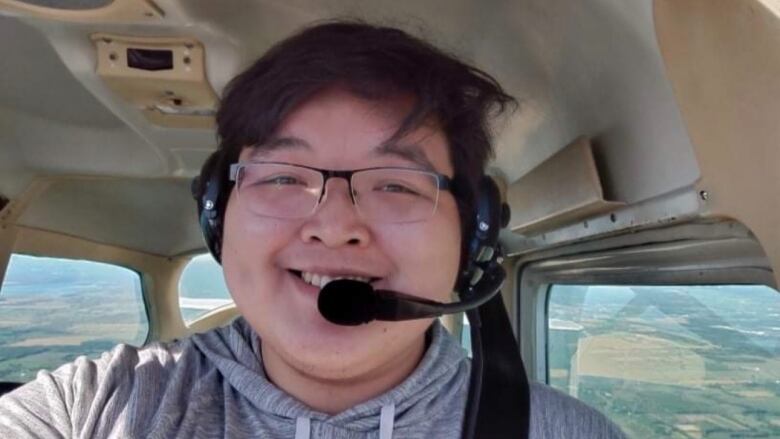 a young man wearing a microphone headset is seated in a plane that is in the air