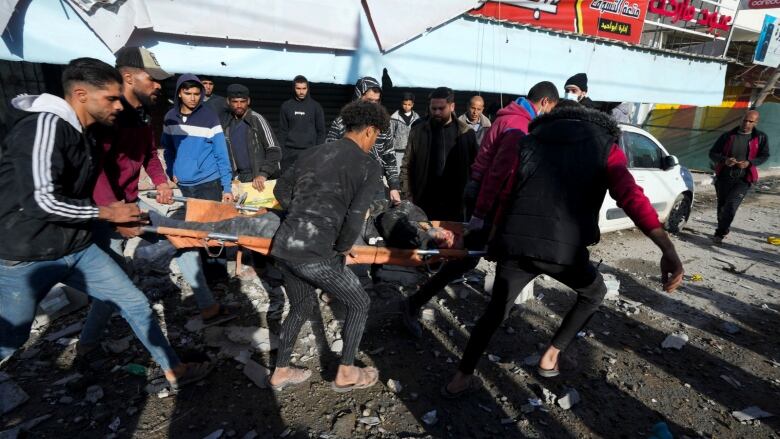 A groupe of people carry a man in a stretcher through a rubble filled street.