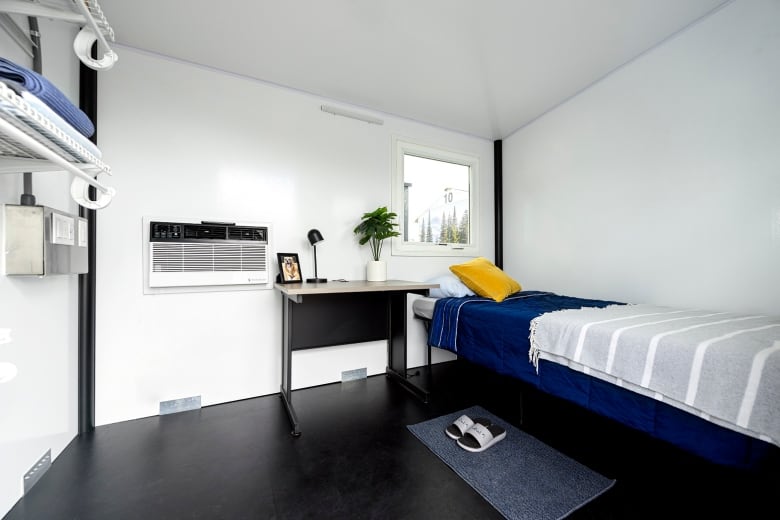 A small bed, desk and shelf can be seen inside a tiny emergency shelter.